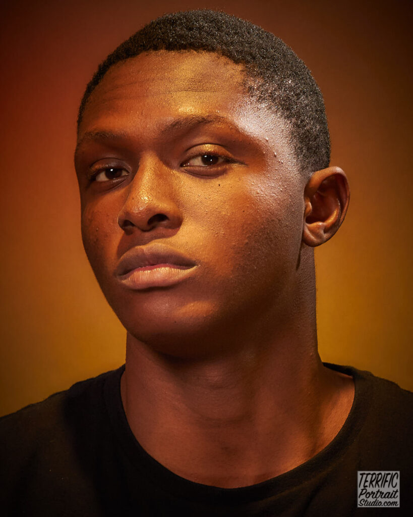 Portrait of Toluwanimi Tunde with short hair, wearing a dark brown shirt on a brown background taken at the Terrific Portrait Studio in Ottawa, ON by Jim Miles